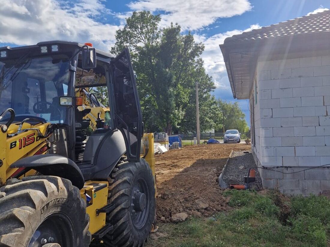 Traktorbáger New Holland B115D pri zásype a urovnaní terénu okolo novostavby