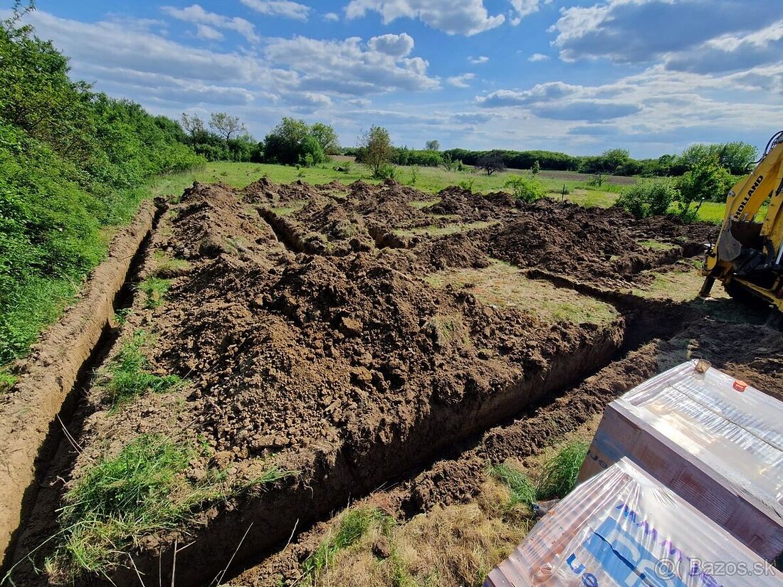 Vykopané základové pásy pre rodinný dom s pripraveným stavebným materiálom